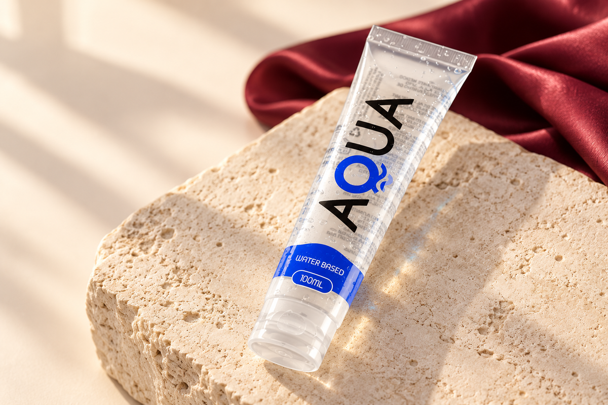 Clear AQUA 100 ml water-based lubricant tube on pale limestone with burgundy fabric behind it.